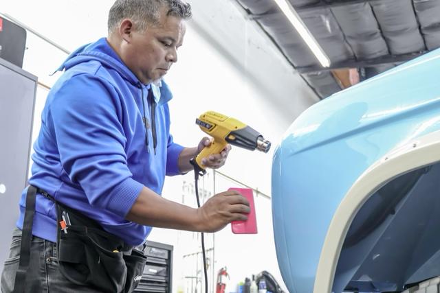 Installer using a heat gun and squeegee on a light blue truck